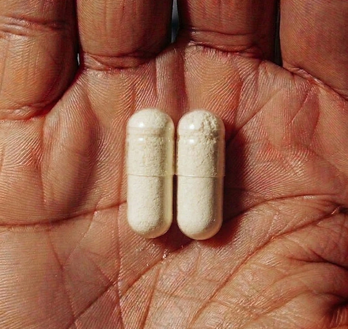 Two beige BoulderBio digestive enzyme capsules resting in an open hand.