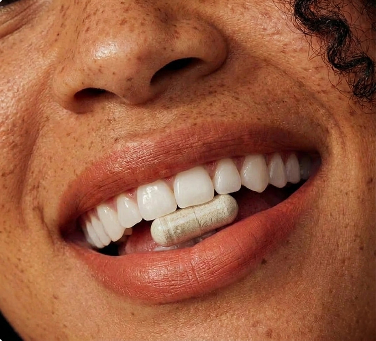 Close-up of a person holding a digestive enzyme capsule between their teeth.