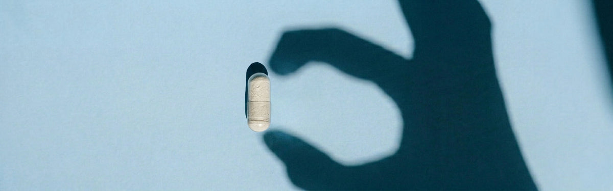 Shadow of hand holding an enzyme capsule against a light blue background